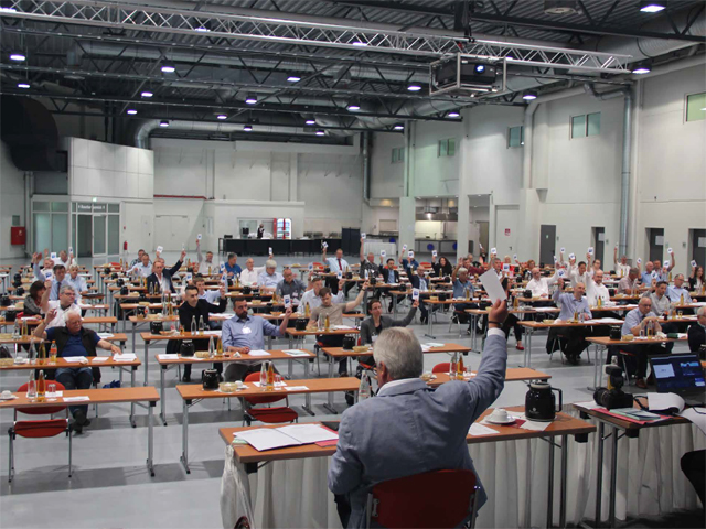 VdB Vertreter sitzen in einem großen Konferenzsaal an Tischen und nehmen an einer Abstimmung beim Gewerkschaftstag teil.